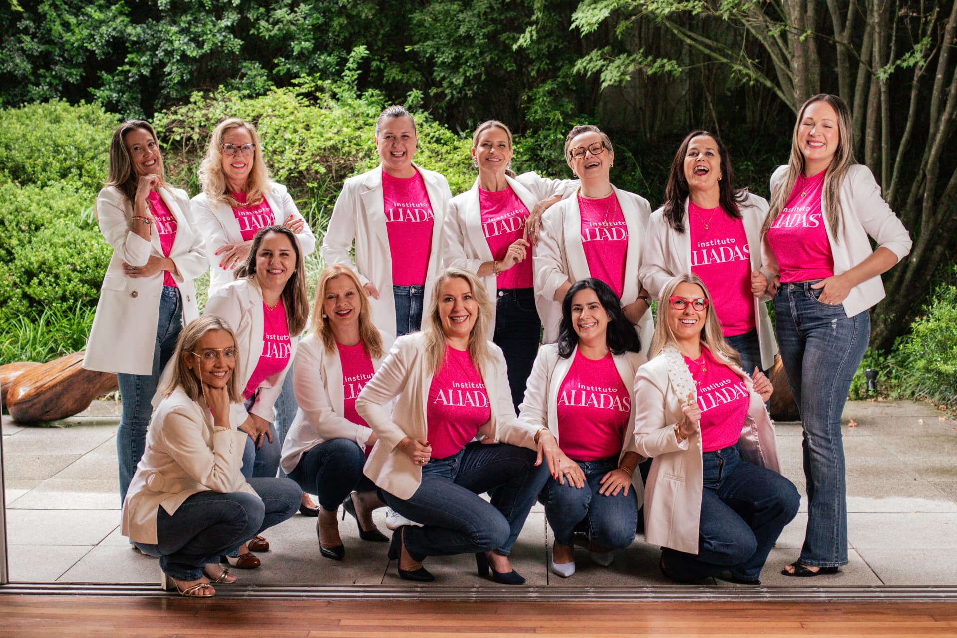 Foto coletiva da equipe do Instituto Aliadas posando ao ar livre, vestindo blazers brancos sobre camisetas pink com o logo do Instituto