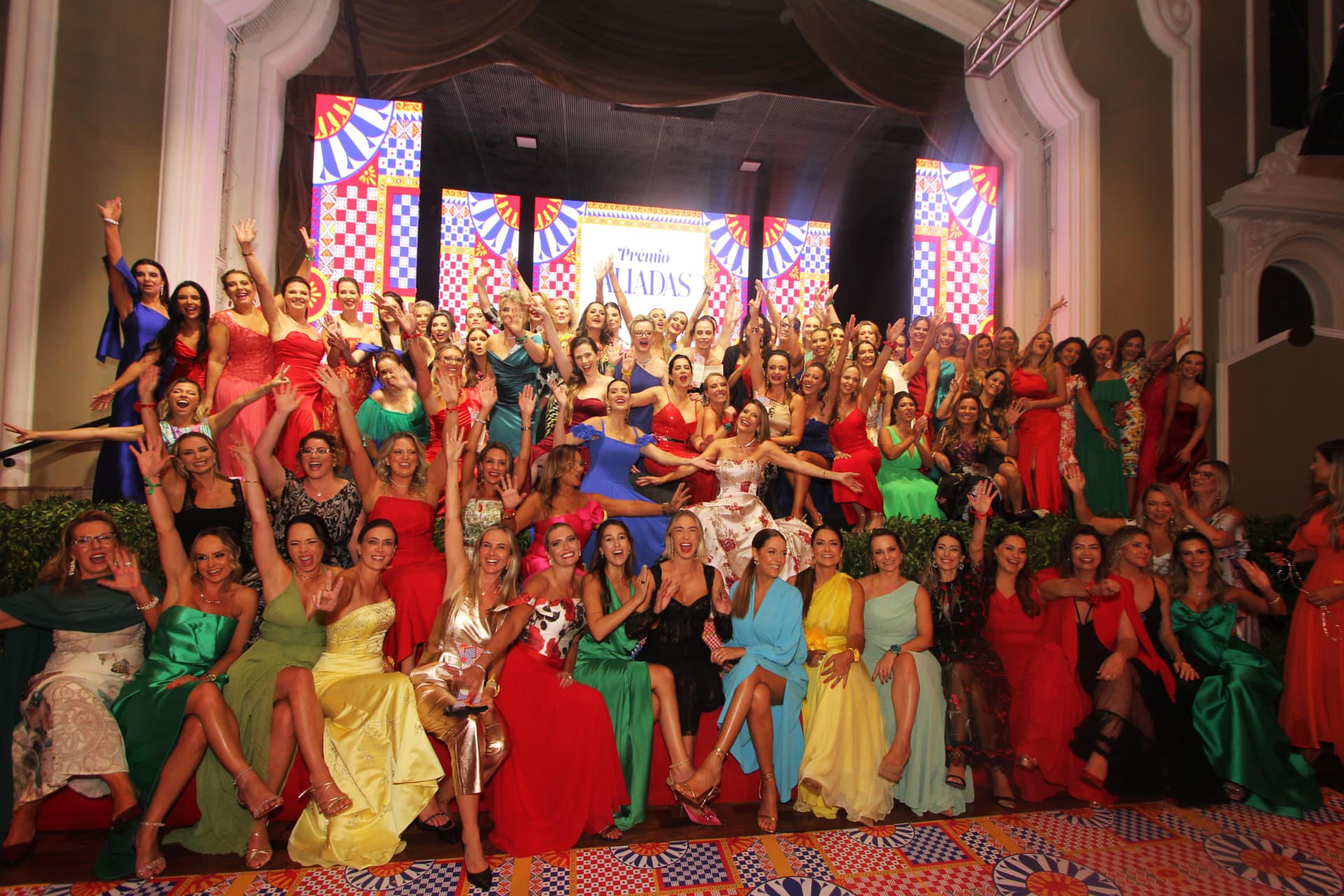 Foto coletiva das homenageadas do Prêmio Aliadas 2025 no palco, com vestidos coloridos e o cenário inspirado na Sicília